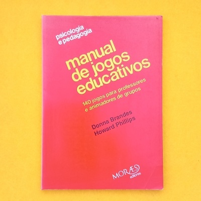 Livro vermelho 'manual de jogos educativos' com texto amarelo e preto sobre fundo amarelo.