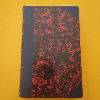 Livro com capa dura vermelha e preta textura marmoreada e cantos azuis sobre fundo amarelo