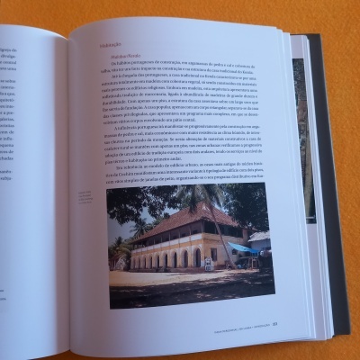 Livro aberto com texto em português e foto de prédio antigo com telhado vermelho