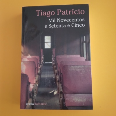 Capa do livro 'Mil Novecentos e Setenta e Cinco' de Tiago Patrício com imagem de bancos violetas e corredor interior de transporte