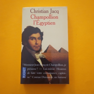 Capa do livro 'Champollion l'Égyptien' de Christian Jacq com retrato e pirâmides
