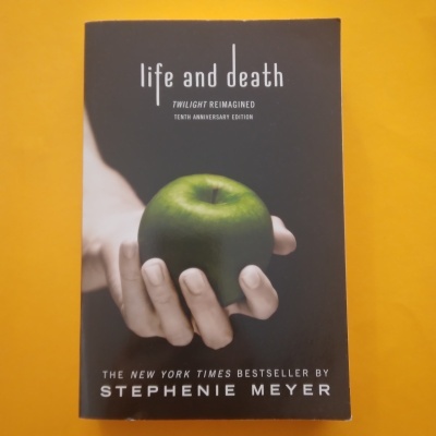 Livro 'life and death' com capa preta, mão segurando maçã verde