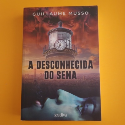 Capa do livro 'A DESCONHECIDA DO SENA' de Guillaume Musso com ilustração de farol e rosto de mulher