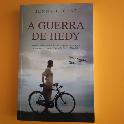 Capa de livro A Guerra de Hedy com pessoa e bicicleta e aviões no céu