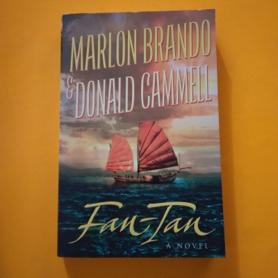 Capa de livro Fan-Tan com barco de velas vermelhas e texto em fundo laranja