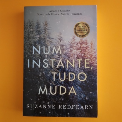 Capa do livro 'Num instante, tudo muda' com árvores nevadas, texto em branco e dourado e selo dourado de prémio