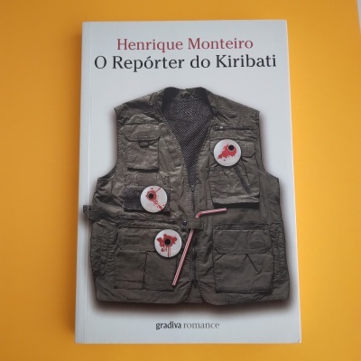 Capa do livro 'O Repórter do Kiribati' de Henrique Monteiro com imagem de colete verde com bottons vermelhos, fundo laranja.