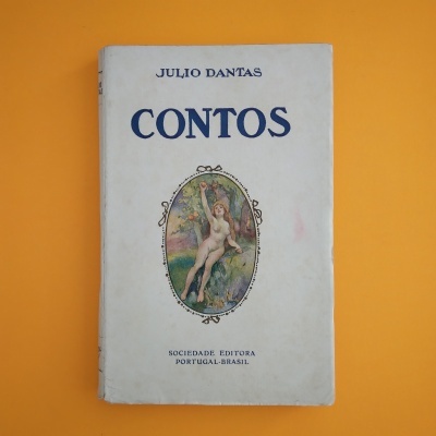 Livro 'CONTOS' de Julio Dantas com capa branca e ilustração central, sobre fundo laranja