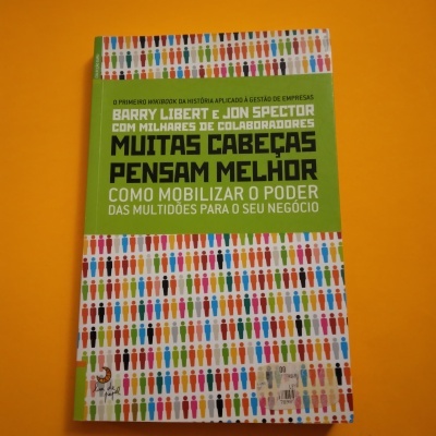 Livro 'Muitas Cabeças Pensam Melhor' com capa verde e figuras humanas coloridas, sobre fundo laranja