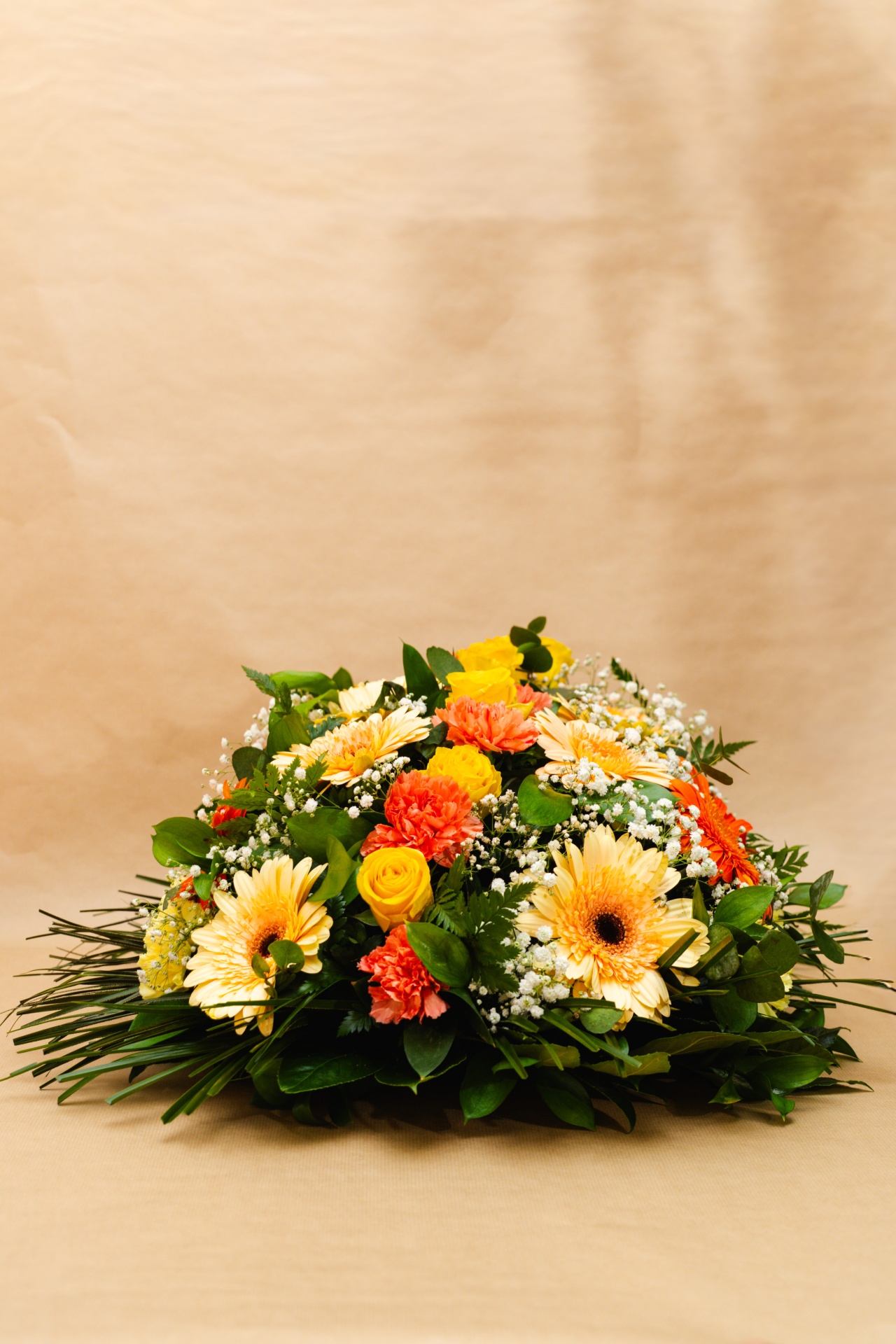 Arranjo floral com rosas amarelas, cravos laranja, margaridas creme e folhagem verde
