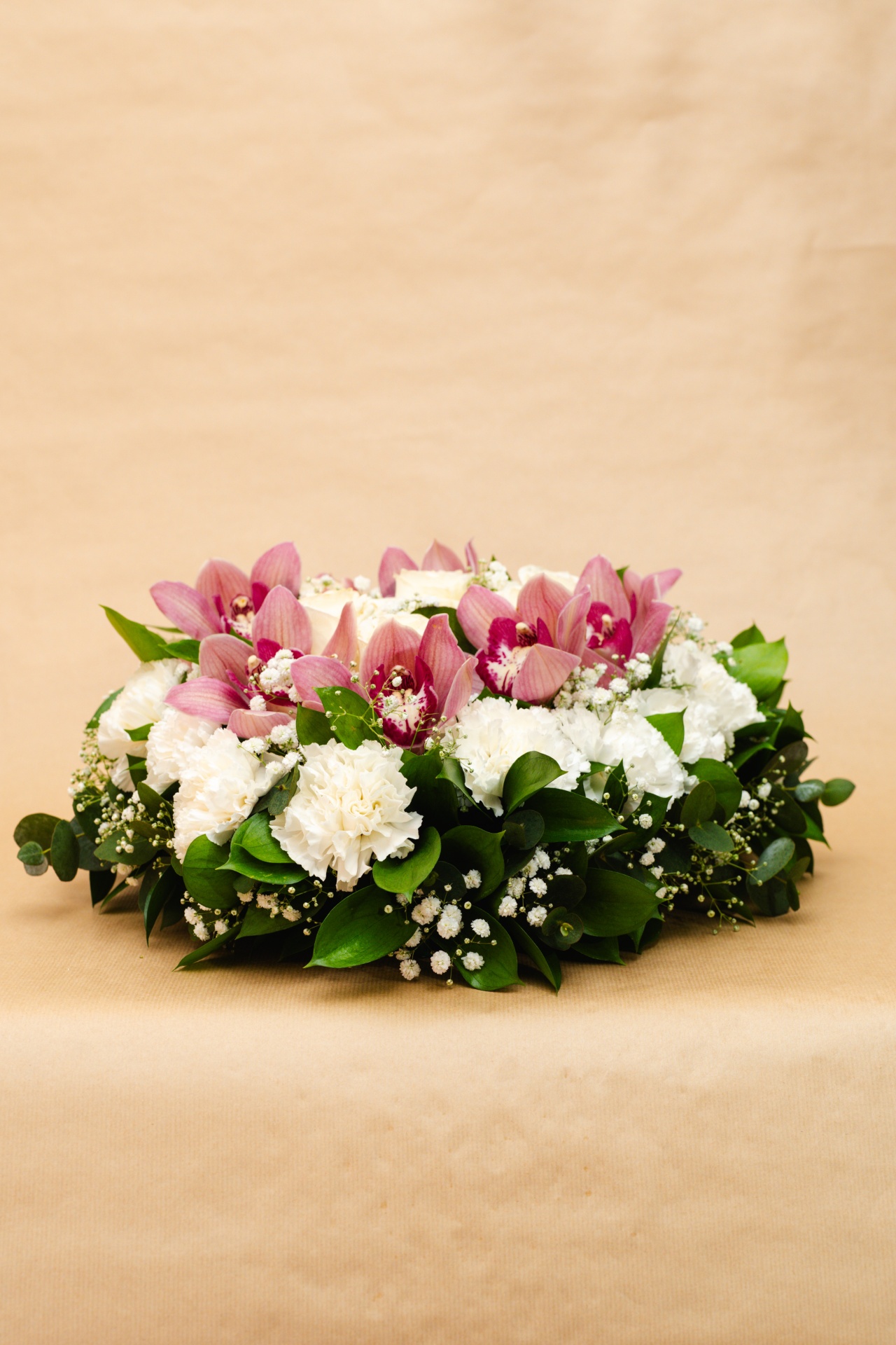Arranjo floral branco e rosa com folhas verdes sobre fundo bege