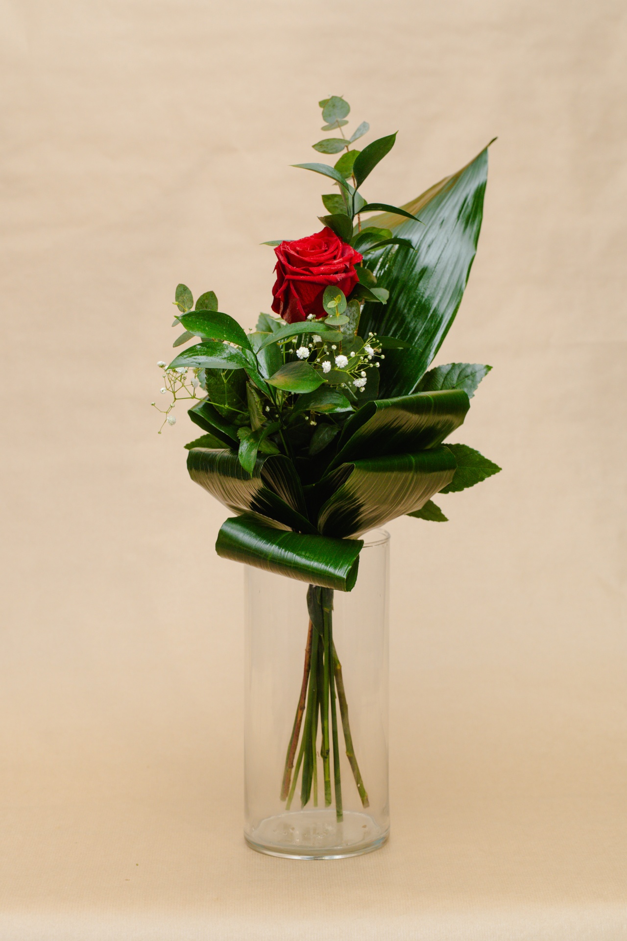 Flor única vermelha com folhas verdes num vaso de vidro cilíndrico