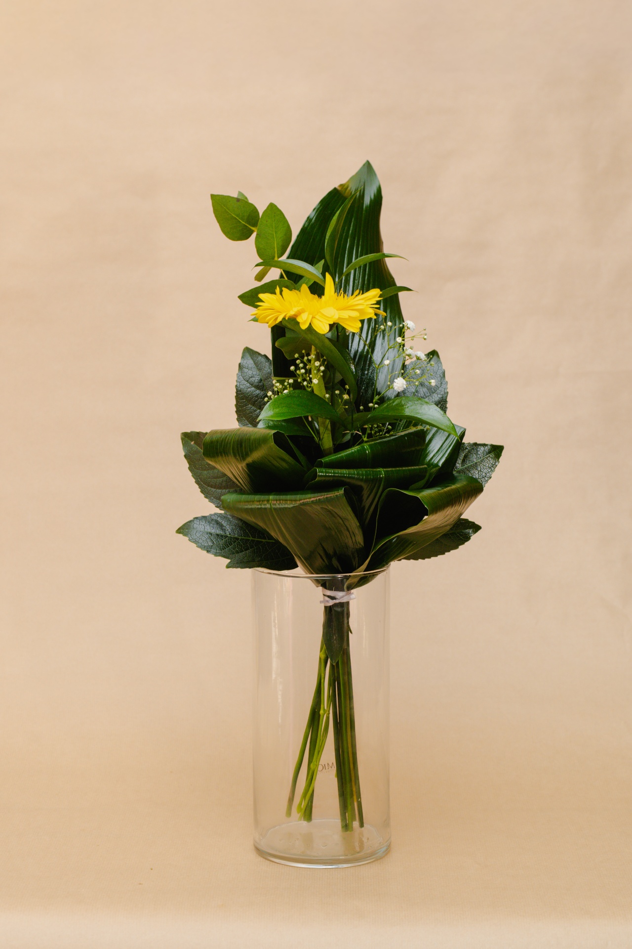 Ramo de flores amarelas e folhas verdes em vaso de vidro transparente