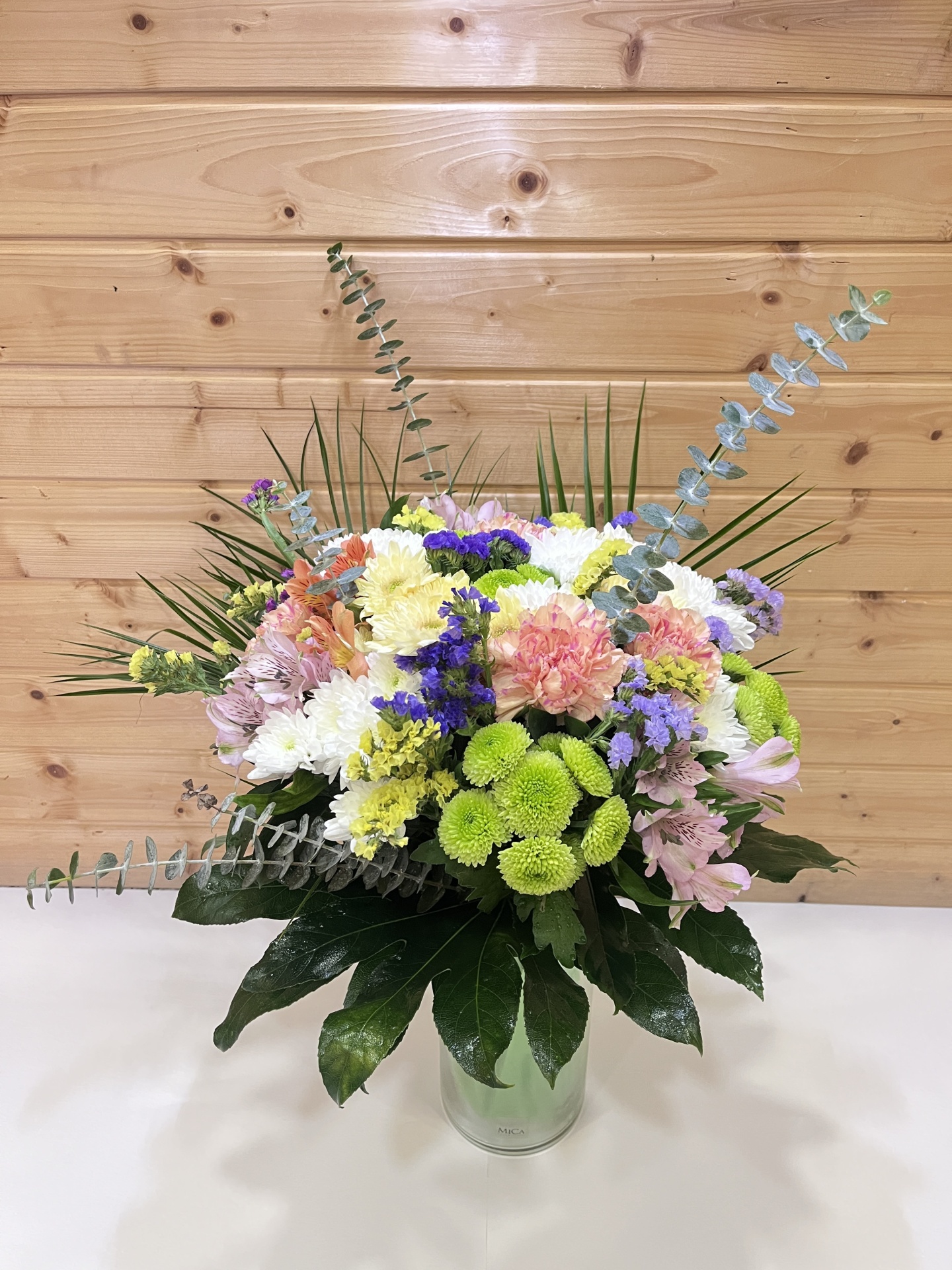 Arranjo floral colorido em vaso de vidro com fundo de madeira clara