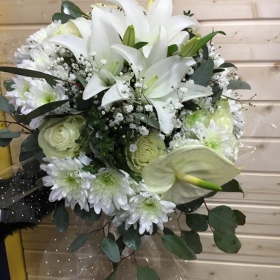 Buquê de flores brancas com lírios, crisântemos, rosas e folhagem em fundo de madeira clara