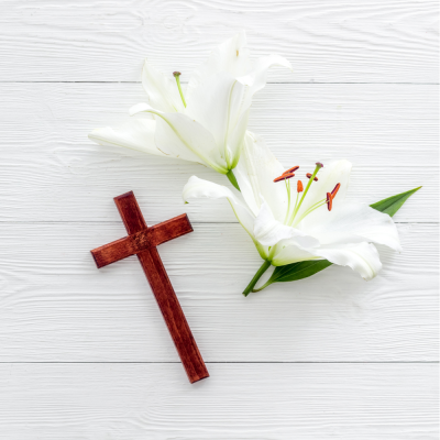 Cruz de madeira castanha com duas flores de lírio brancas sobre madeira branca
