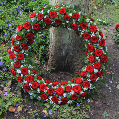 Coroa circular de flores vermelhas e brancas junto a um tronco de árvore