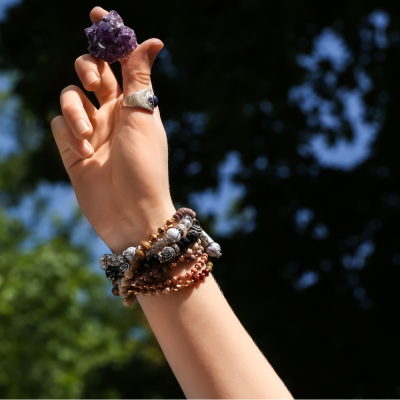 Mão com pulseiras e anel segurando cristal roxo ao ar livre