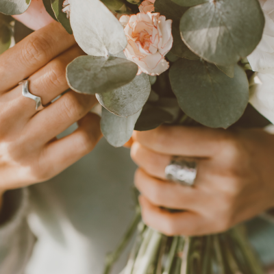 Pessoa com anéis prateados segurando ramo de flores brancas e rosas