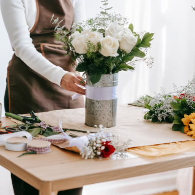 Arranjo de flores com rosas brancas num vaso metálico cinzento numa mesa de madeira.