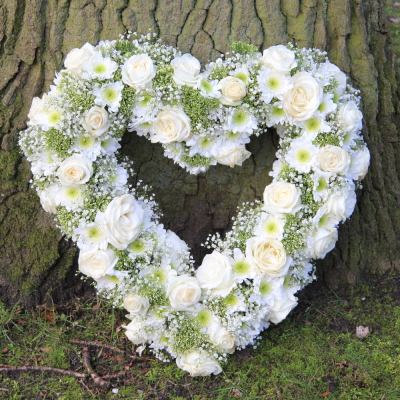 Aliança floral em formato de coração com flores brancas e verdes encostada a uma árvore