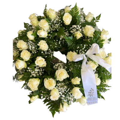 Coroa funebre com rosas brancas, folhas verdes e laço branco com texto.