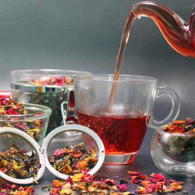 Chá a ser servido em chávena de vidro com folhas e pétalas em recipientes de vidro.