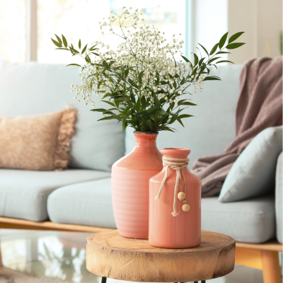 Dois jarros cor de rosa com flores em mesa de madeira em sala de estar
