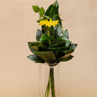 Ramo de flores amarelas e folhas verdes em vaso de vidro transparente