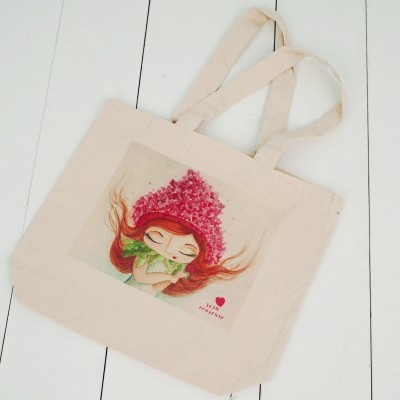 Saco de tecido cru com ilustração colorida de rapariga com gorro de flores e texto 'I LOVE TRAVEL'.