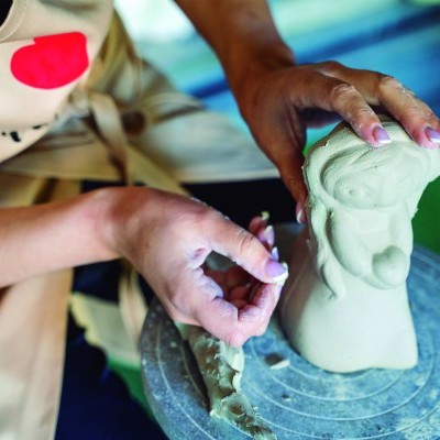 Pessoa a moldar peça de cerâmica verde clara numa roda de oleiro azul
