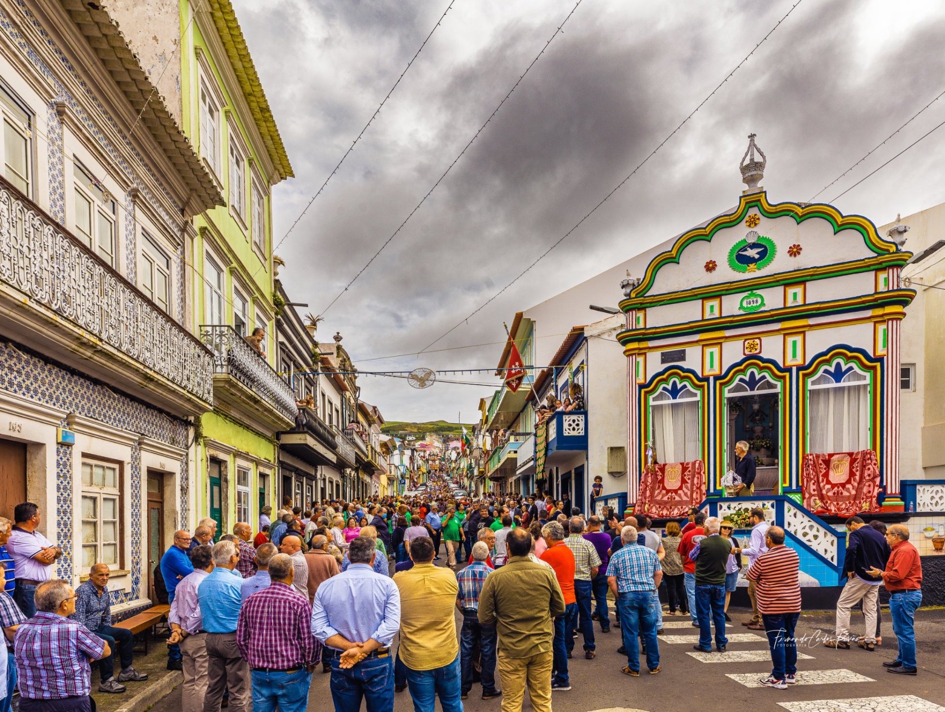 Rua antiga com pessoas e edifícios coloridos ao fundo sob céu nublado