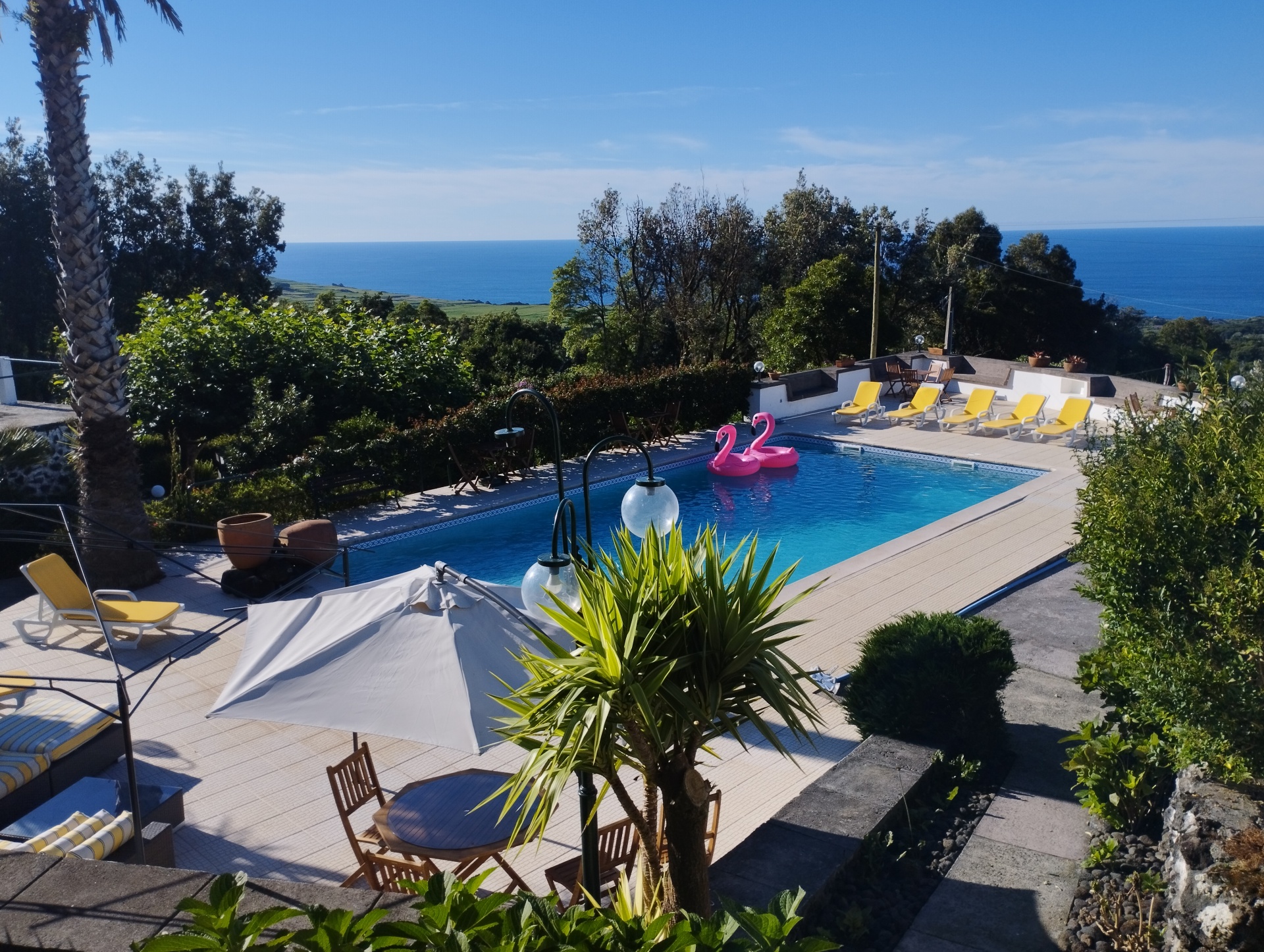 Piscina exterior com espreguiçadeiras amarelas e vista para o mar