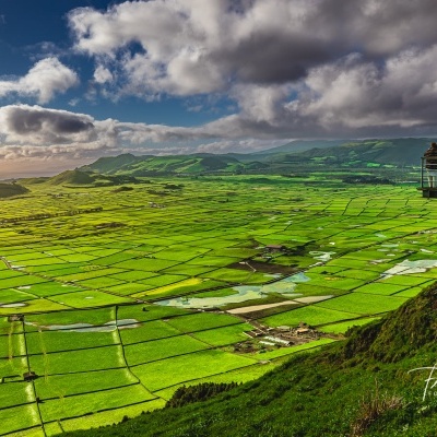 Campos verdes agrícolas vistos de uma colina com pessoas em plataforma de observação sob céu nublado