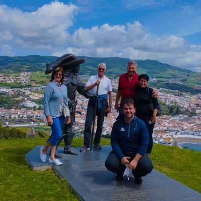 Cinco pessoas junto a estátua de bronze numa área verde com vista para cidade e mar