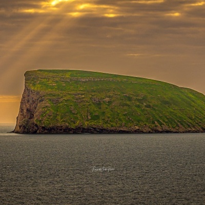 Ilha rochosa verde rodeada de água sob céu com raios de sol