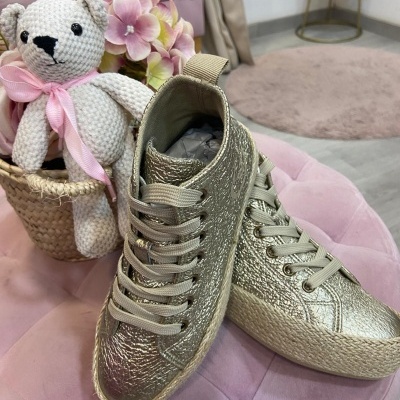 Ténis dourados infantis com ursos de crochet e flores ao lado em fundo interior