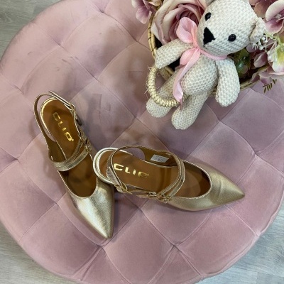 Sapatos dourados de salto médio sobre almofada rosa com flores e ursinho de pelúcia