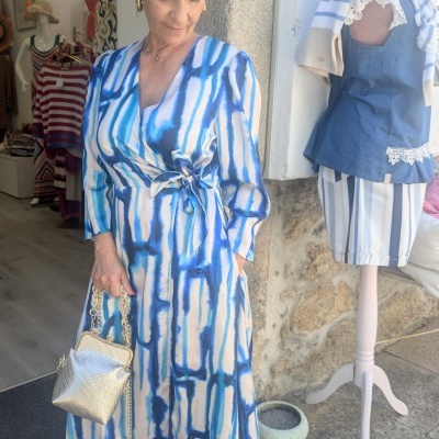 Mulher com vestido longo azul e branco e mala dourada junto a manequim com roupa azul e branca