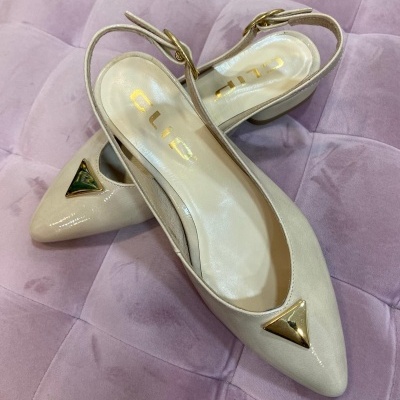 Sapatos de senhora bege com salto médio e detalhes dourados sobre almofada rosa