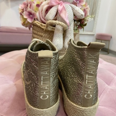 Ténis dourados Chatta com sola de corda sobre almofada rosa, decorados com flores e ursinho de crochê ao fundo.