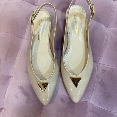 Sapatos slingback bege com detalhes metálicos sobre sofá lilás.