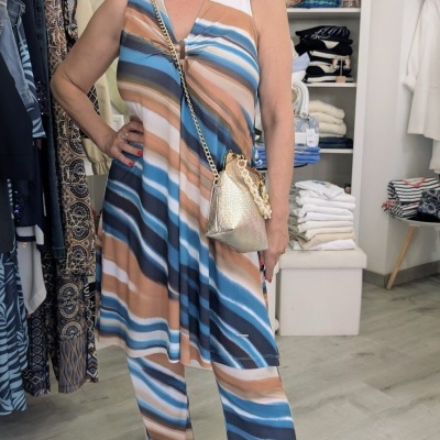 Mulher com conjunto de vestido e calças às riscas com bolsa dourada em loja de roupa