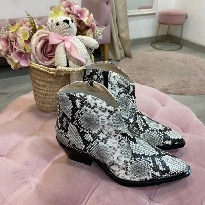 Botas com padrão pele de cobra em pufe rosa com vaso de flores e urso de peluche ao fundo