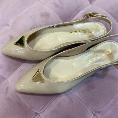 Par de sapatos femininos creme com detalhes dourados sobre almofada rosa claro