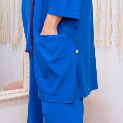 Conjunto azul com casaco e calças largas, botões coloridos e bolso, em interior decorado com mandalas.