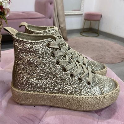 Ténis dourados de cano alto sobre sofá cor-de-rosa