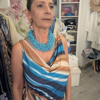 Mulher com vestido listrado azul e bege e colar azul claro em loja de roupas