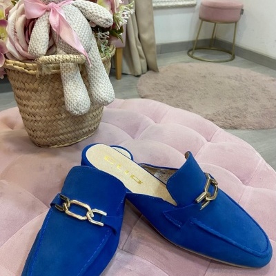 Mules azuis em camurça com fivela dourada sobre puff rosa e ursos em cesta de verga