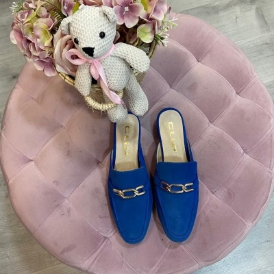 Mules azuis com detalhe dourado, ursinho de crochê branco e flores em almofada rosa